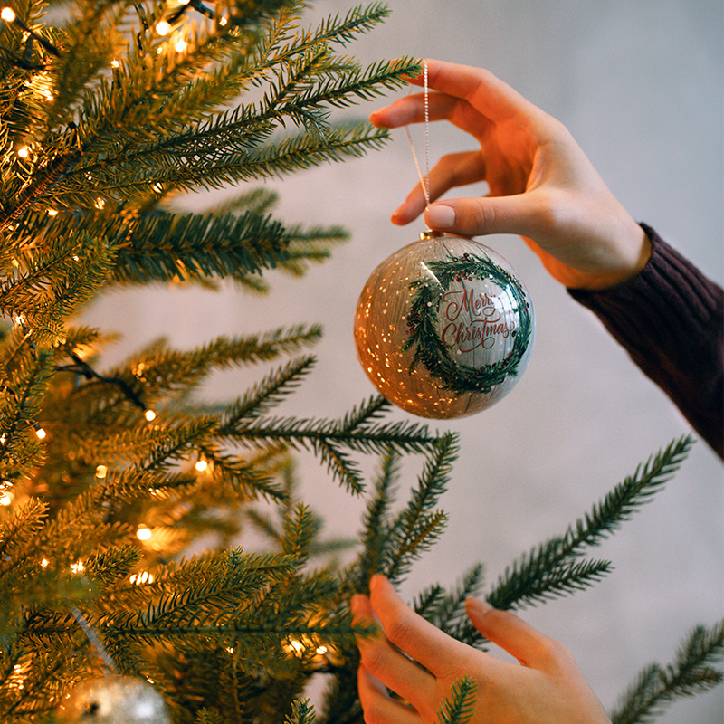 A person is decorating the Christmas tree with Christmas balls