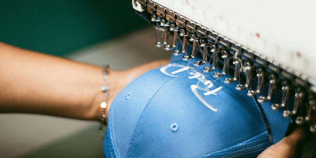 An embroidery machine is embroidering a blue hat