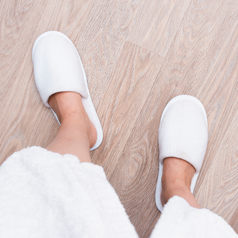 A person is walking on a wooden floor wearing a pair of pure white slippers